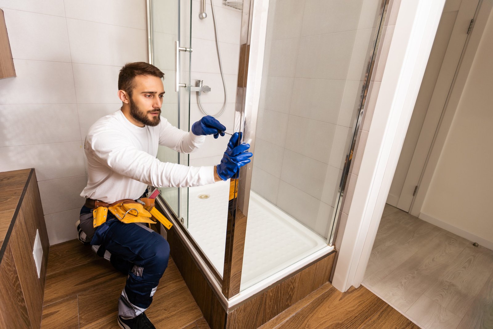 The worker is connecting the glass walls of the shower enclosure with a metal bar