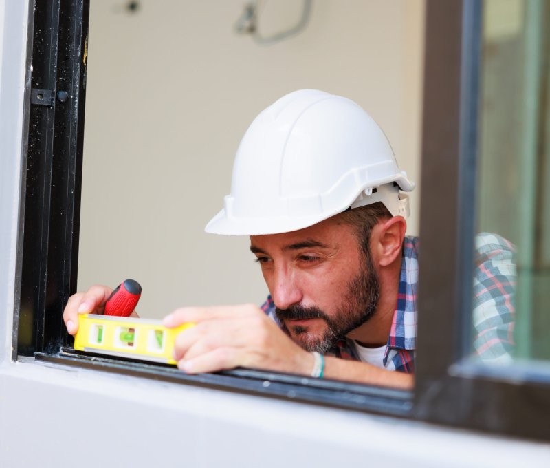 Man installing windows in  new house construction site. Hispanic Construction worker wearing protect gloves and hardhat helmet